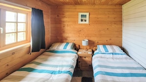 A cabin with two beds, wooden walls, a window with curtains, a small table with a lamp, and a framed picture on the wall. - 2 bedroom accommodation in Kippford near Dalbeattie (Kippford near Dalbeattie)