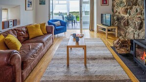 A cozy living room with a brown leather sofa, a blue armchair, a wooden coffee table, and a stone fireplace. - 1 bedroom accommodation in Clynnog Fawr (Clynnog Fawr)