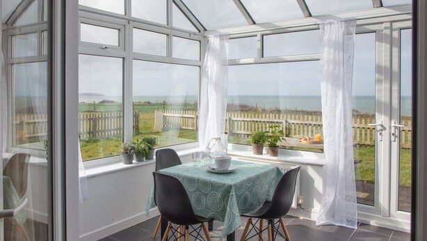 A conservatory with a table and chairs, potted plants, and a view of a fence and fields. - 1 bedroom accommodation in Clynnog Fawr (Clynnog Fawr)