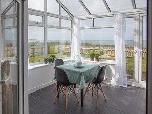 Een oranjerie met een tafel, stoelen, potplanten en uitzicht op een hek en velden.