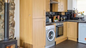 A modern kitchen with wooden cabinets, a stove, a washing machine, and a dishwasher. - 1 bedroom accommodation in Clynnog Fawr (Clynnog Fawr)