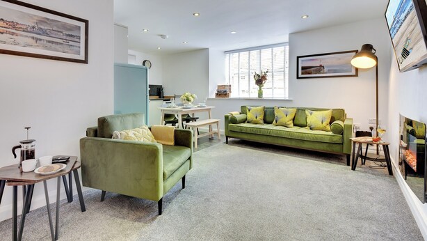 A modern living room with a green sofa, a coffee table, and a dining area. - 2 bedroom accommodation in Berwick-upon-Tweed (Berwick-upon-Tweed)