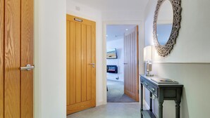 A hallway with wooden doors, a mirror, a console table, and a view into a bedroom with a bed and a TV. - 2 bedroom accommodation in Berwick-upon-Tweed (Berwick-upon-Tweed)