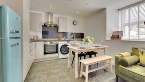 A compact kitchen with modern appliances, a dining area with a bench, and a view of the outside through a window. - 2 bedroom accommodation in Berwick-upon-Tweed (Berwick-upon-Tweed)