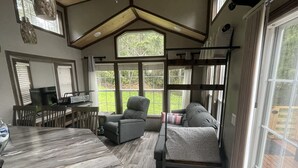 Une pièce chaleureuse avec un plafond en bois, un canapé, un fauteuil, une table et de grandes fenêtres donnant sur l’extérieur.