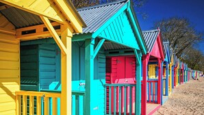 Une rangée de cabanes de plage colorées, dotées de balustrades en bois, avec une plage de sable en arrière-plan.
