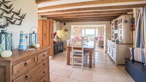Une cuisine spacieuse avec des poutres en bois, un coin repas avec des chaises et une vue dégagée par une porte ouverte.