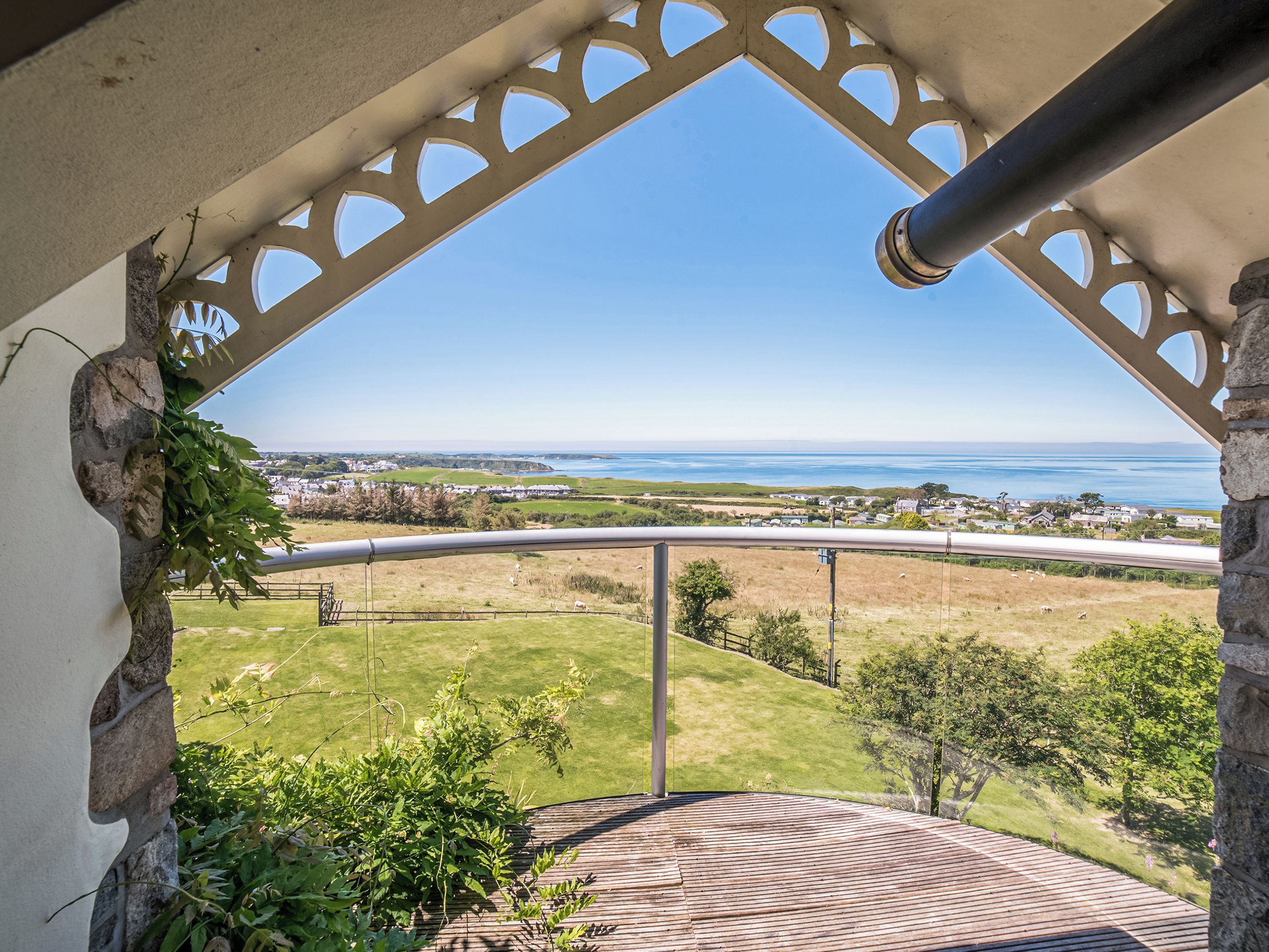 Un balcon donnant sur un paysage côtier, une terrasse dallée et un mur en pierre.