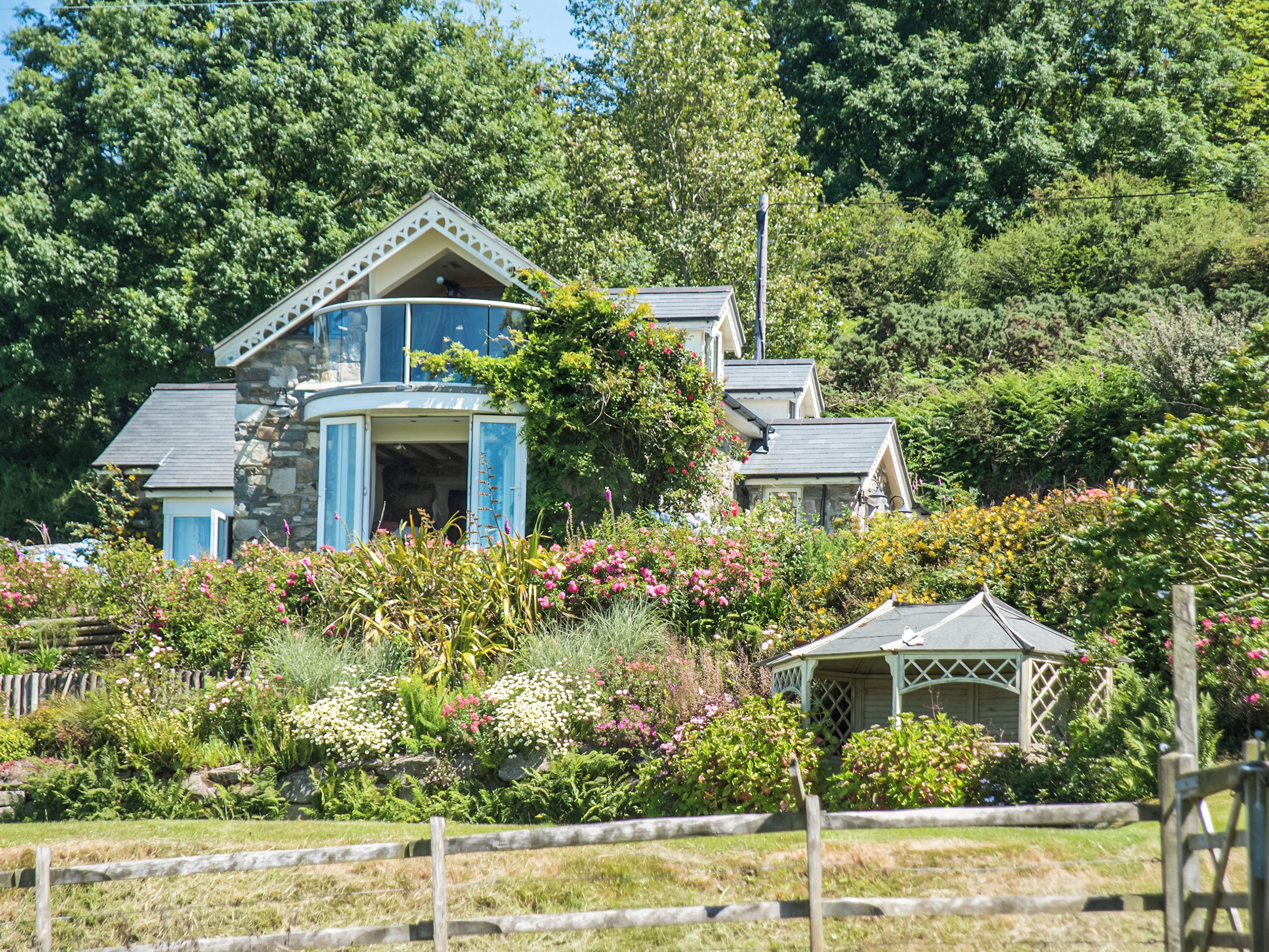 Une maison à deux étages avec une façade en pierre, une porte bleue et un petit kiosque dans le jardin.