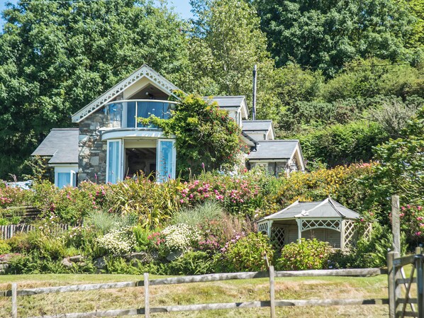 A two-story house with a stone facade, a blue door, and a small gazebo in the front yard.