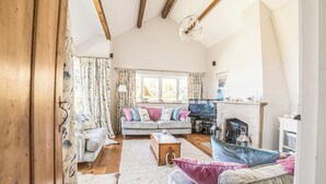 A cozy living room with a fireplace, wooden beams, and a sofa with colorful cushions.