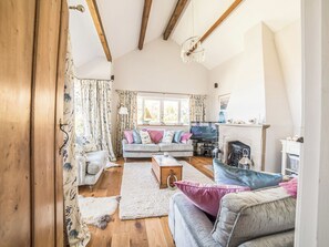 A cozy living room with a fireplace, wooden beams, and a sofa with colorful cushions.