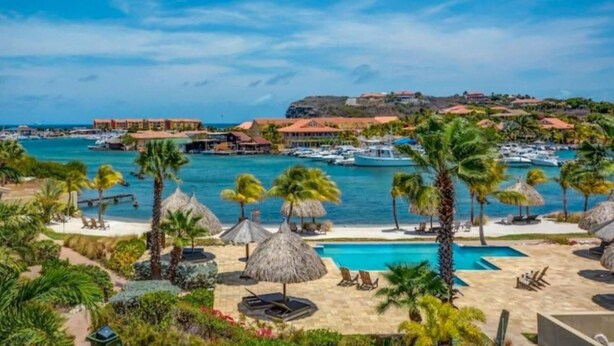 A resort with a pool, palm trees, and a view of the sea and buildings. - Appartement La Maya met Zwembad Strand Jan Thiel (Jan Thiel)