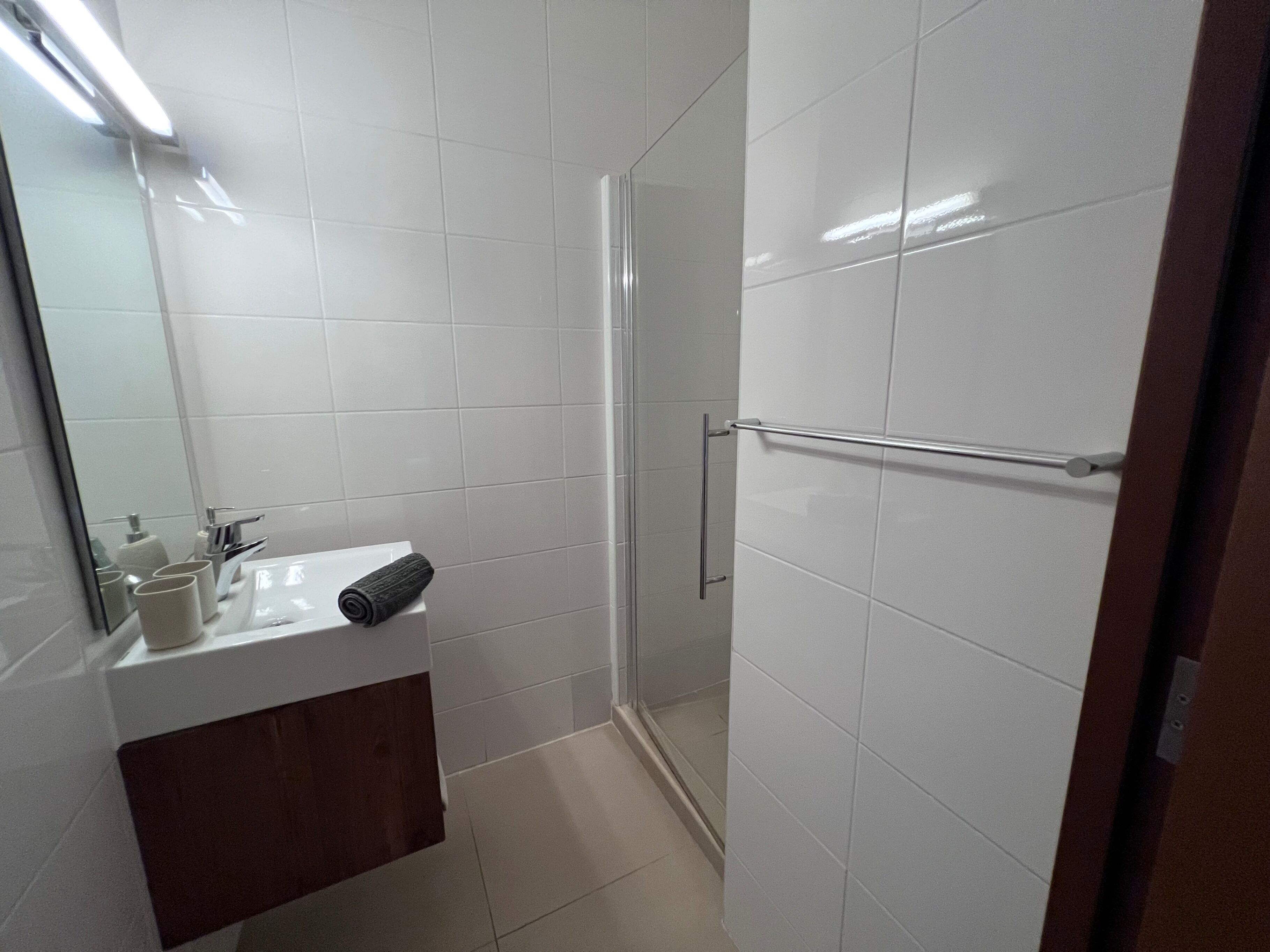 Een moderne badkamer met witte tegels, een houten wastafelmeubel, een douchecabine met glas en een handdoekrek.