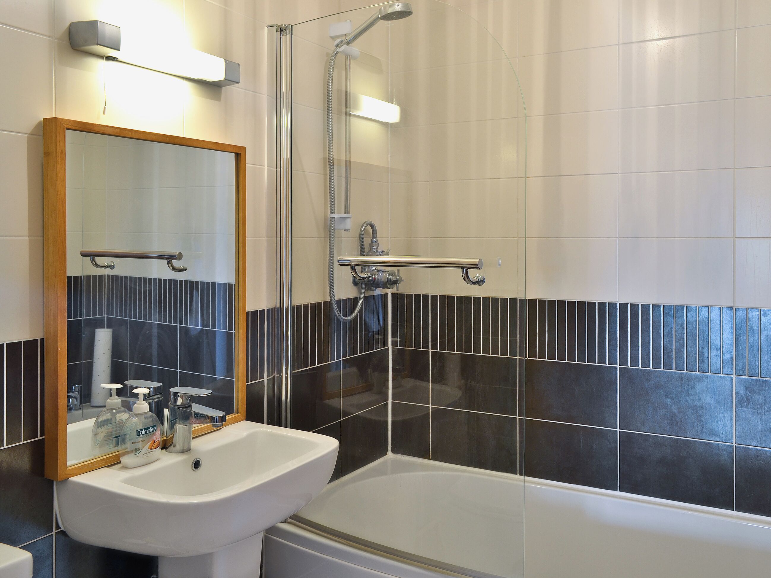 Uma casa de banho moderna com lavatório branco, espelho, cabine de duche e paredes com mosaico preto e branco.