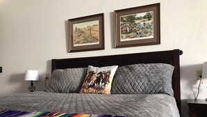 A bed with a grey quilt, two pillows with cowboy images, and two framed pictures on the wall. - Katie's Cozy Suites (Tombstone)
