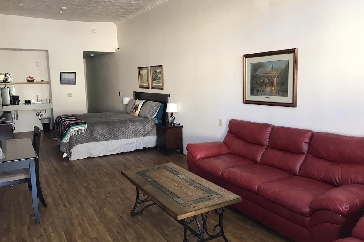 A bedroom with a bed, bedside tables, a red sofa, a wooden coffee table, and a desk with a chair.
