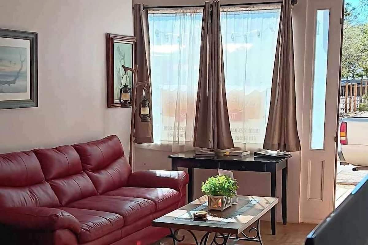 A room with a red sofa, a small table with a plant, a TV, and large windows with curtains.