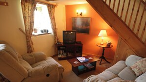 A cozy living room with a sofa, a recliner, a coffee table with books, a television, and a lamp. - Nestled in a prime location with spectacular views over open countryside. (Staintondale near Scarborough)