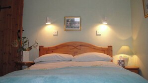 A bedroom with a wooden bed, two bedside lamps, a nightstand with a lamp, a wall-mounted picture, and a wooden door. - Nestled in a prime location with spectacular views over open countryside. (Staintondale near Scarborough)