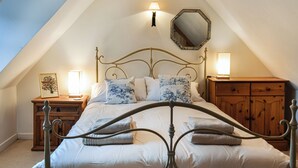 Een slaapkamer met een schuine kap, een metalen bedframe, een houten dressoir en twee bedlampen.