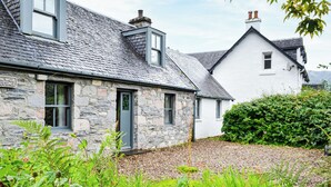 Een stenen cottage met een grijs dak, een kleine tuin en een bordje met de tekst 'Kirk Wood Cottage'.