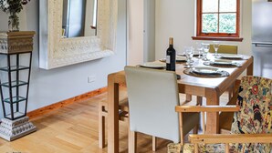 Een eethoek met een houten tafel voor vier personen, een spiegel met een versierlijk lijstwerk en een raam met uitzicht op groen.