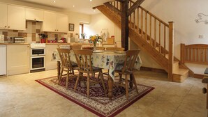 A kitchen with white cabinets, a wooden staircase, and a dining area with a table and chairs. - 3 bedroom accommodation in Cold Eaton, Alsop-en-le-Dale (Cold Eaton, Alsop-en-le-Dale)