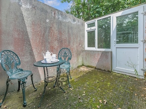 A small outdoor seating area with a table and two chairs, a white door, and a window.
