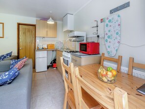 Una cocina compacta con un microondas rojo, una estufa y un lavamanos. Hay una mesa de comedor con sillas y un tazón de fruta.