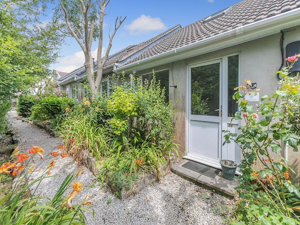 A house with a tiled roof, a gravel pathway, and various plants and flowers.