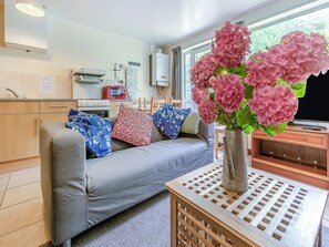 Una cocina moderna con un sofá gris, un jarrón con flores rosadas y una mesa de madera con una rejilla metálica.