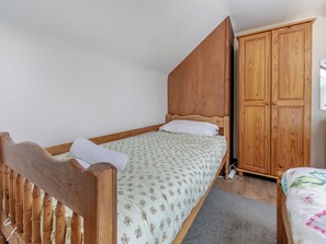 Una cama individual con cabecera de madera, un armario de madera y una alfombra gris.