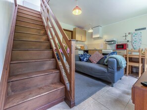 Una escalera conduce a un espacio de sala de estar con sofá, una mesa de comedor y una cocina al fondo.
