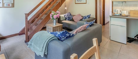 Ein Wohnzimmer mit Sofa, Holzstuhl, kleinem Tisch, Küchenbereich und einer Treppe.