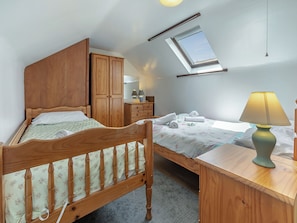 A bedroom with two wooden beds, a skylight, a bedside table with a lamp, and a wardrobe.