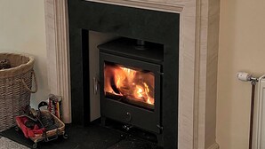 A room with a stone fireplace, a basket, and a radiator.