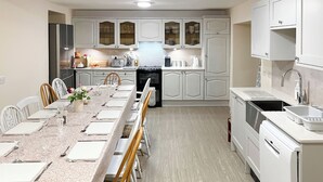 A modern kitchen with white cabinetry, a long dining table set for six, and a built-in oven.
