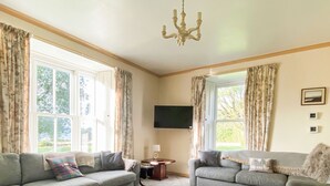 A living room with two grey sofas, a white rug, and a chandelier.