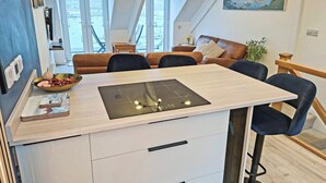 A modern kitchen with a central island, a dining area with a brown leather sofa, and a view of a cityscape through large windows. - 2 bedroom accommodation in Kingswear (Kingswear)
