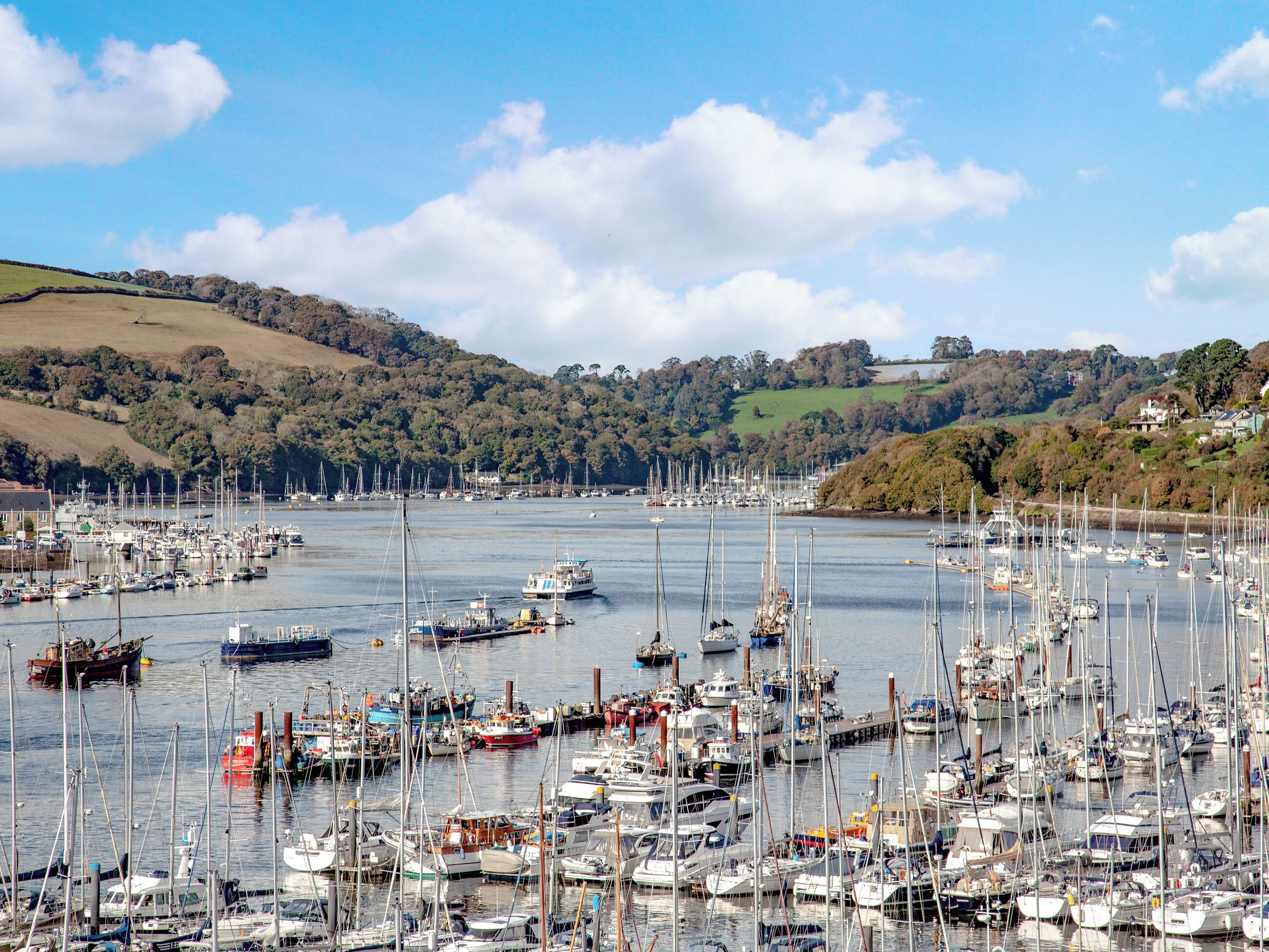 A marina filled with various boats and yachts, surrounded by hills and a clear sky.