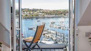 A view from a balcony with a wooden chair, overlooking a marina with boats and a town in the background. - 2 bedroom accommodation in Kingswear (Kingswear)