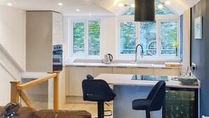 A modern kitchen with a large window, a dining area with two chairs, and a staircase. - 2 bedroom accommodation in Kingswear (Kingswear)