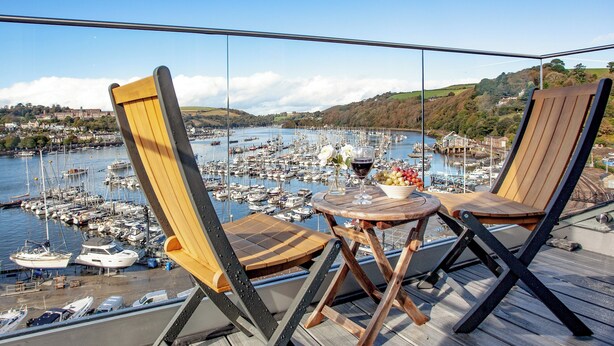 A balcony with two wooden chairs and a small table, overlooking a marina with numerous boats. - 2 bedroom accommodation in Kingswear (Kingswear)