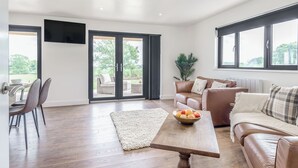 A spacious living area with a wooden coffee table, leather sofas, and a large window. - Oak Tree Lodge - UK38383 (Lyonshall, near Kington)