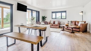 A spacious living area with a dining table, sofa, and large windows offering a view of the outdoors. - Oak Tree Lodge - UK38383 (Lyonshall, near Kington)