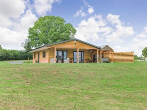 A wooden cabin with a covered patio, large windows, and a grassy lawn. - Oak Tree Lodge - UK38383 (Lyonshall, near Kington)