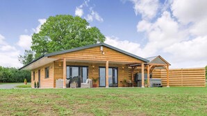 A modern wooden house with a covered porch, a fenced backyard, and a large tree. - Oak Tree Lodge - UK38383 (Lyonshall, near Kington)
