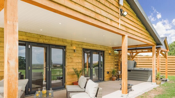 A covered patio with wicker furniture, a hot tub, and a view of the surrounding landscape. - Oak Tree Lodge - UK38383 (Lyonshall, near Kington)