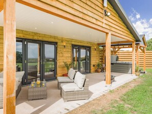 A covered patio with wicker furniture, a hot tub, and a view of the surrounding landscape. - Oak Tree Lodge - UK38383 (Lyonshall, near Kington)
